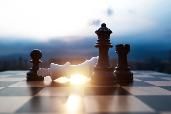 Chess pieces depicting a black queen, rook and pawn checkmating a white king.